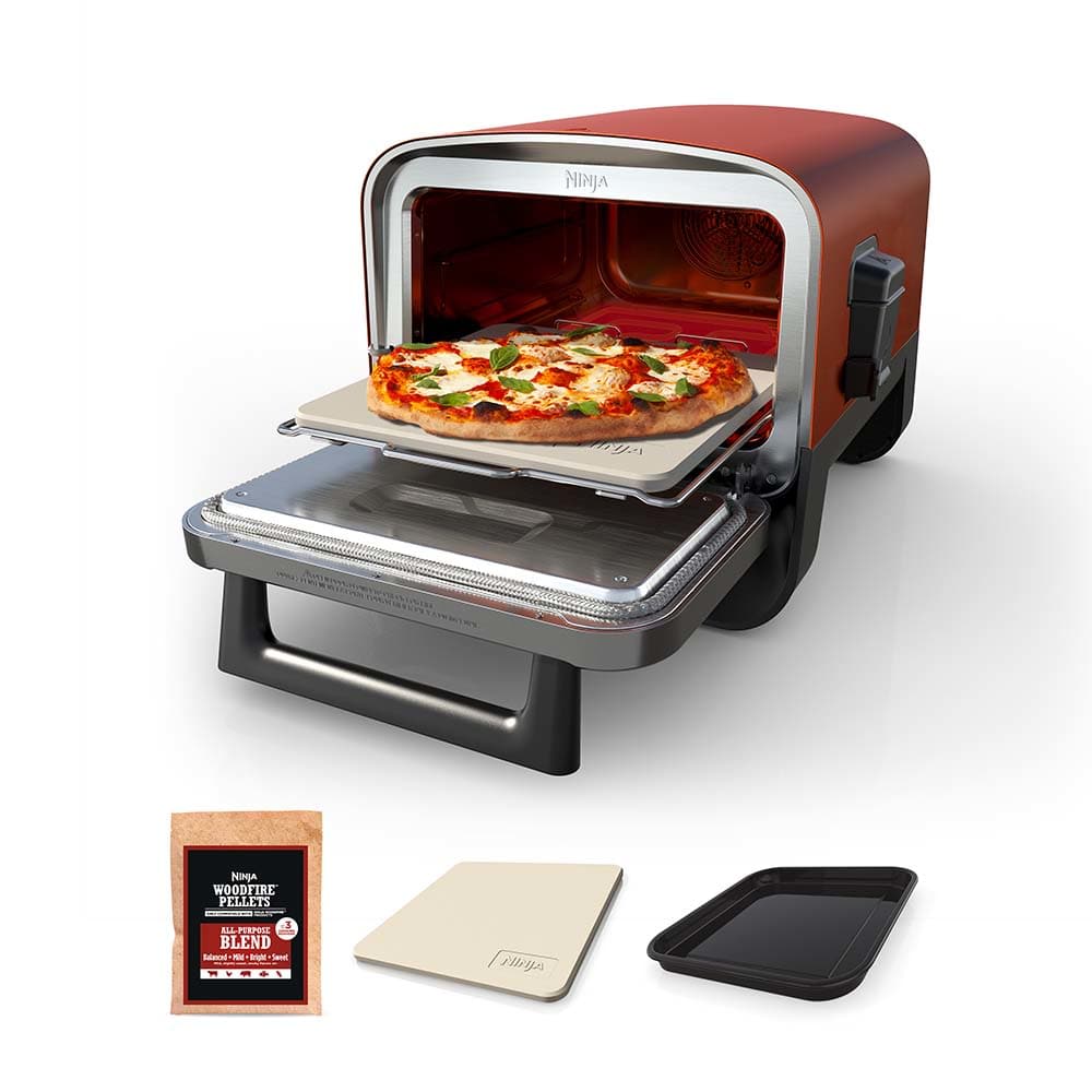 Ninja Woodfire Pizza Oven model OO101 shown open with pizza on its stone and the supplied pan and accessory pieces nearby