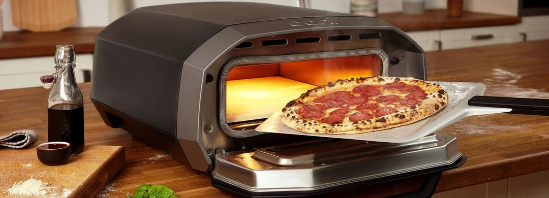Ooni Volt 12 earlier three-dial oven with its door open and a pizza on a peel
